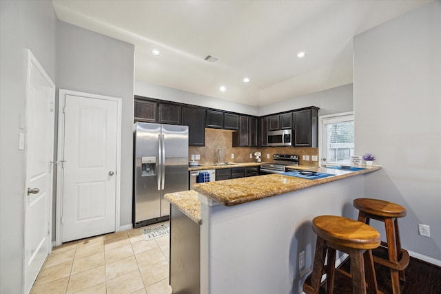 kitchen featuring visible vents, appliances with stainless steel finishes, a peninsula, light stone countertops, and a sink