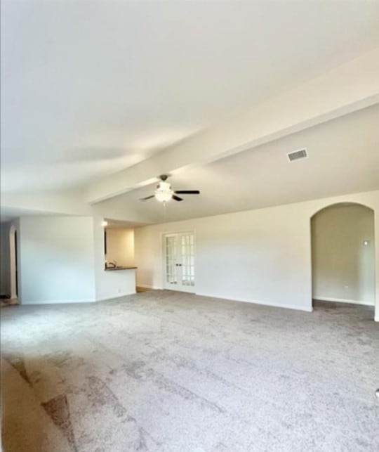 unfurnished living room featuring a ceiling fan, arched walkways, beam ceiling, and carpet