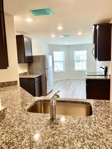 kitchen with light stone counters, light wood finished floors, a sink, dark brown cabinets, and baseboards