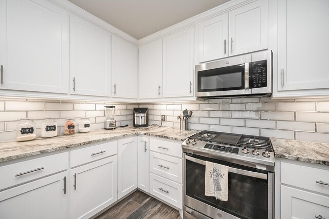 kitchen featuring dark wood-type flooring, white cabinetry, appliances with stainless steel finishes, decorative backsplash, and light stone countertops