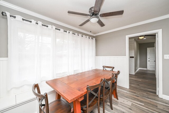 dining area with dark wood-style flooring, wainscoting, a ceiling fan, and crown molding