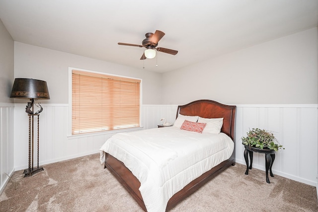 bedroom featuring a wainscoted wall, a ceiling fan, and light colored carpet