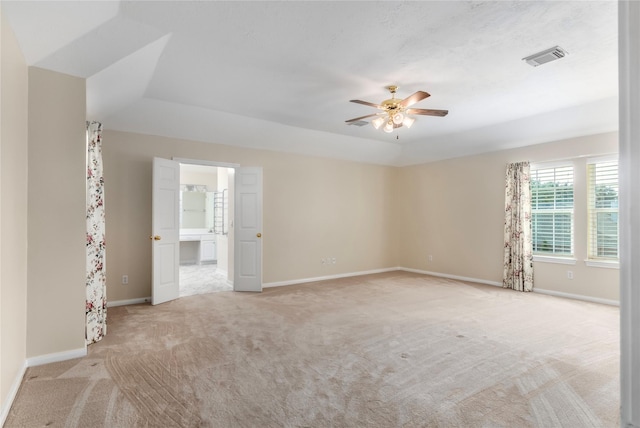 spare room featuring light carpet, ceiling fan, and a raised ceiling