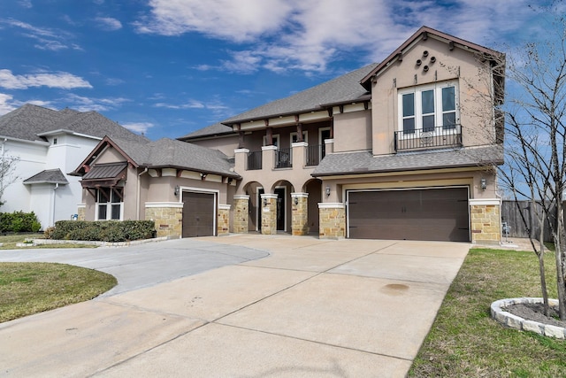 view of front of home with stucco siding, a shingled roof, a balcony, stone siding, and driveway