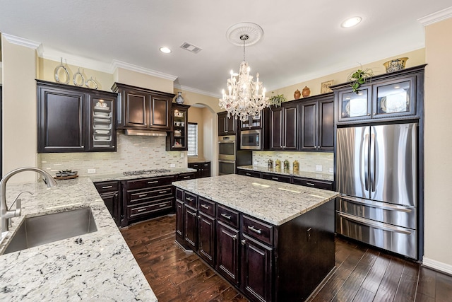 kitchen featuring arched walkways, dark wood-style flooring, stainless steel appliances, crown molding, and a sink