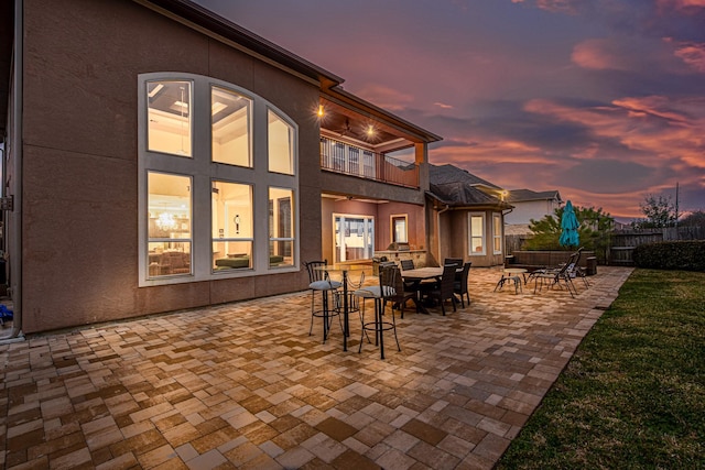 patio terrace at dusk featuring a balcony, fence, and outdoor dining space