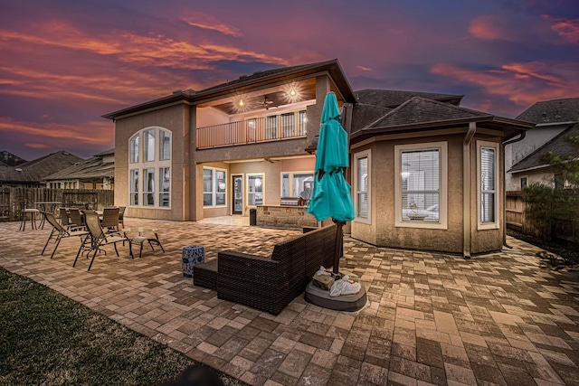 back of property at dusk with a patio, stucco siding, a ceiling fan, a balcony, and a fenced backyard