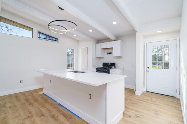 kitchen with black gas stove, light wood-type flooring, white cabinetry, and baseboards