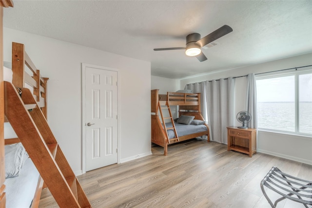 unfurnished bedroom with ceiling fan, a water view, light hardwood / wood-style floors, and a textured ceiling