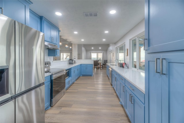 kitchen featuring appliances with stainless steel finishes, sink, light wood-type flooring, blue cabinetry, and decorative light fixtures