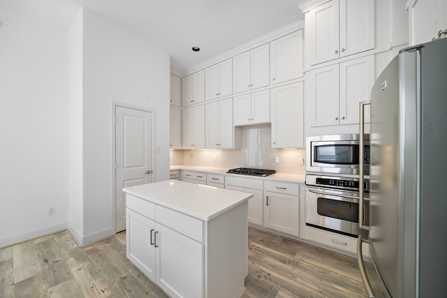 kitchen featuring stainless steel appliances, a center island, white cabinets, light countertops, and decorative backsplash