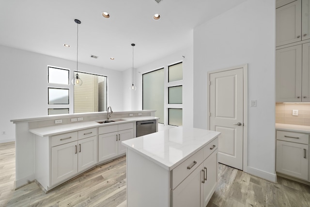 kitchen with light wood-style flooring, a kitchen island, hanging light fixtures, and a sink