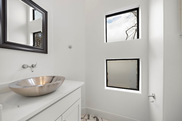 bathroom with marble finish floor, vanity, and baseboards