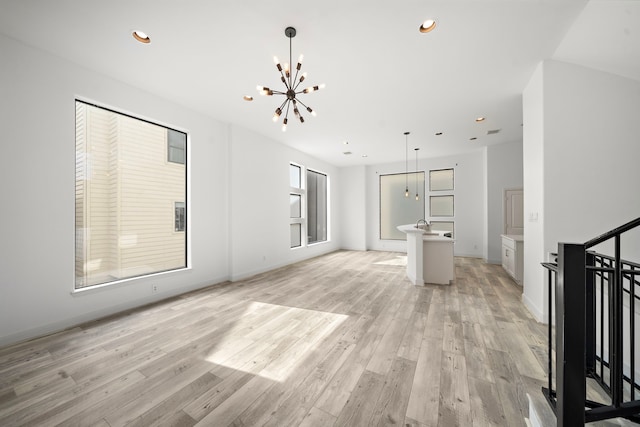 unfurnished living room with light wood-type flooring, a notable chandelier, baseboards, and recessed lighting