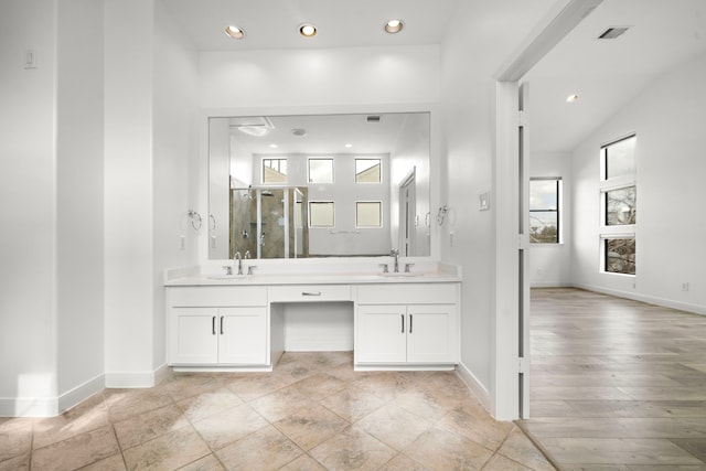 full bathroom featuring double vanity, a stall shower, baseboards, and a sink