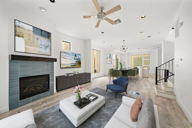 living area featuring visible vents, a tiled fireplace, stairway, light wood-style floors, and recessed lighting