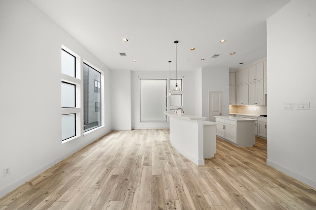 kitchen featuring light wood-style flooring, white cabinetry, light countertops, hanging light fixtures, and a center island with sink