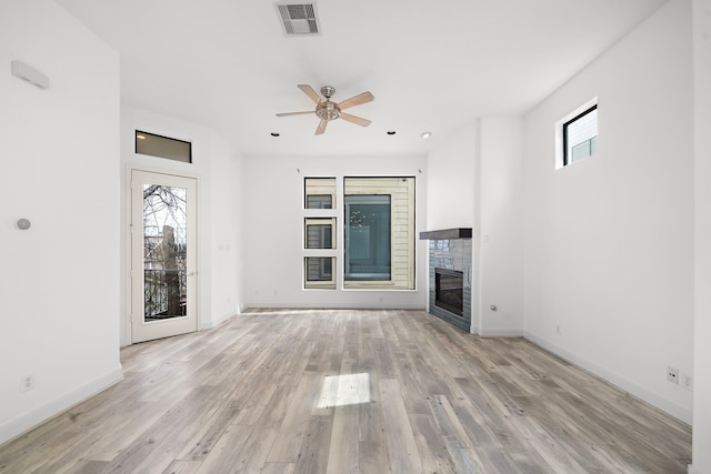 unfurnished living room featuring a ceiling fan, baseboards, visible vents, light wood-style floors, and a tiled fireplace