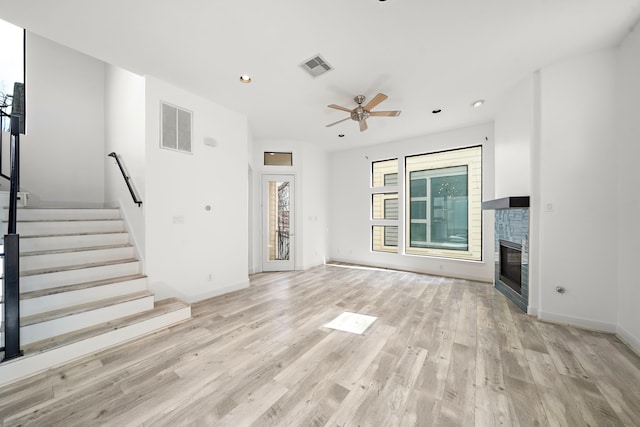 unfurnished living room featuring stairway, visible vents, light wood-style floors, and a glass covered fireplace