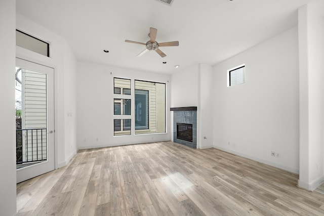 unfurnished living room with ceiling fan, a healthy amount of sunlight, a glass covered fireplace, and light wood-style floors