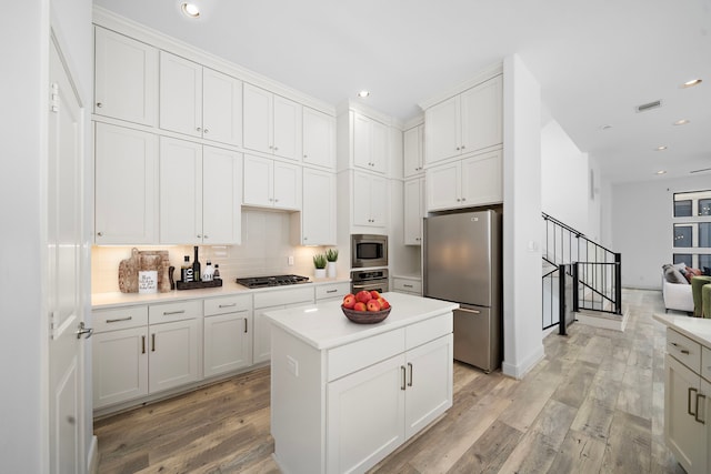 kitchen with light countertops, backsplash, appliances with stainless steel finishes, white cabinetry, and a kitchen island