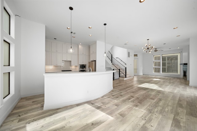 kitchen with white cabinets, open floor plan, hanging light fixtures, stainless steel appliances, and light countertops