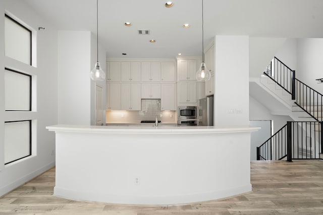 kitchen with hanging light fixtures, stainless steel appliances, light countertops, light wood-style floors, and white cabinetry