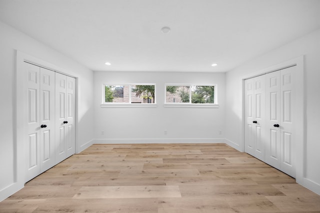 unfurnished bedroom featuring multiple windows, light wood-style flooring, and baseboards