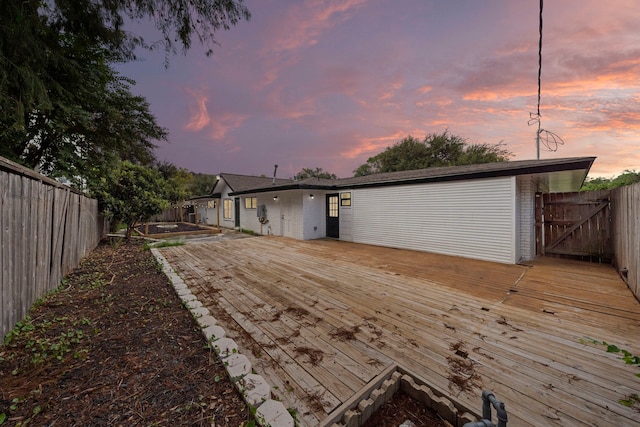 back of house at dusk with a deck, brick siding, and a fenced backyard