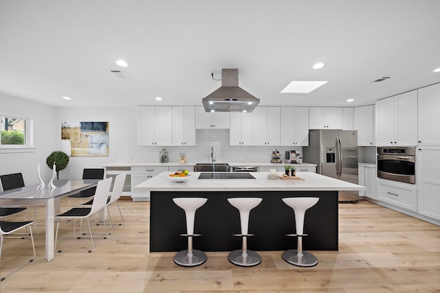 kitchen with a breakfast bar area, island range hood, stainless steel appliances, a kitchen island, and backsplash