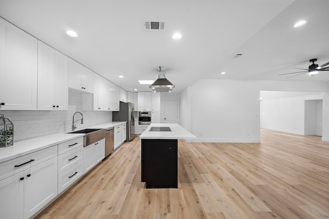 kitchen with a kitchen island, a sink, visible vents, appliances with stainless steel finishes, and tasteful backsplash