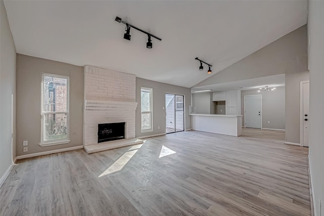 unfurnished living room with rail lighting, light hardwood / wood-style flooring, vaulted ceiling, and a brick fireplace