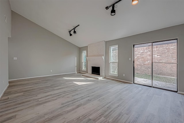 unfurnished living room featuring a fireplace, vaulted ceiling, rail lighting, and light hardwood / wood-style flooring