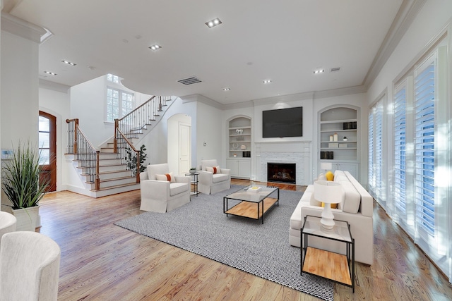 living room featuring a fireplace, ornamental molding, light hardwood / wood-style floors, and built in shelves