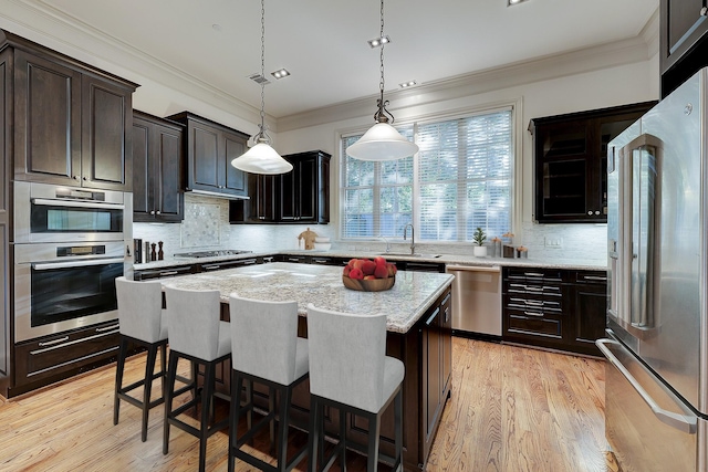 kitchen with a breakfast bar area, stainless steel appliances, pendant lighting, a center island, and light wood-type flooring