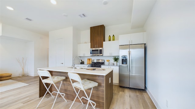 kitchen featuring a center island with sink, stainless steel appliances, light countertops, white cabinets, and a kitchen bar