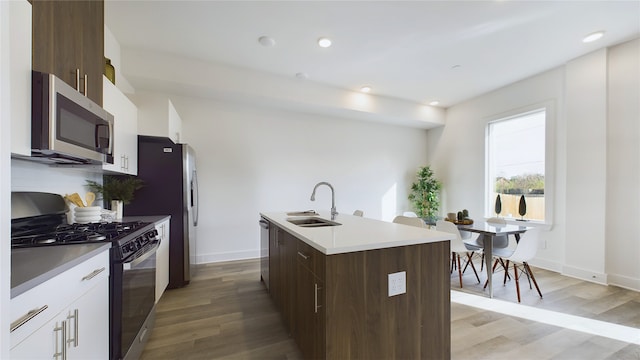 kitchen featuring white cabinets, a kitchen island with sink, stainless steel appliances, light wood-style floors, and a sink