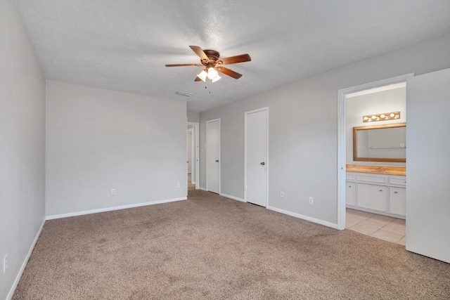 unfurnished bedroom featuring visible vents, light colored carpet, ensuite bathroom, a textured ceiling, and baseboards