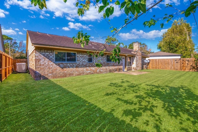 rear view of property with a fenced backyard, a chimney, a lawn, and central AC