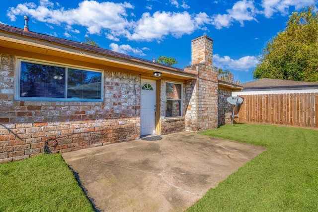 rear view of property with a lawn, a chimney, fence, a patio area, and brick siding