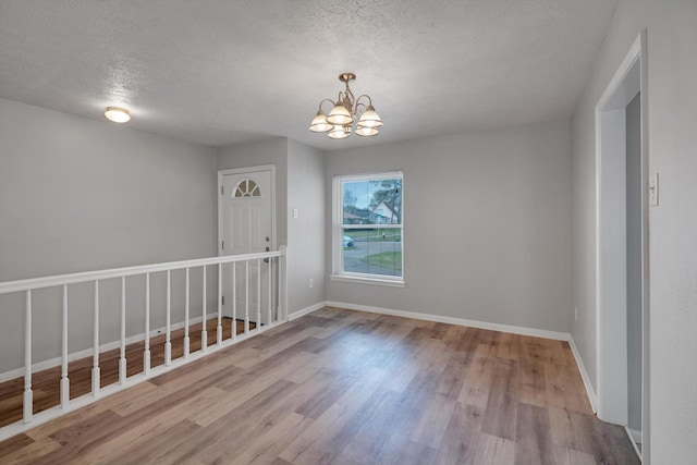 spare room with an inviting chandelier, a textured ceiling, baseboards, and wood finished floors