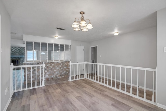 spare room with a fireplace, wood finished floors, visible vents, baseboards, and an inviting chandelier