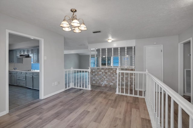 empty room featuring baseboards, a notable chandelier, visible vents, and wood finished floors