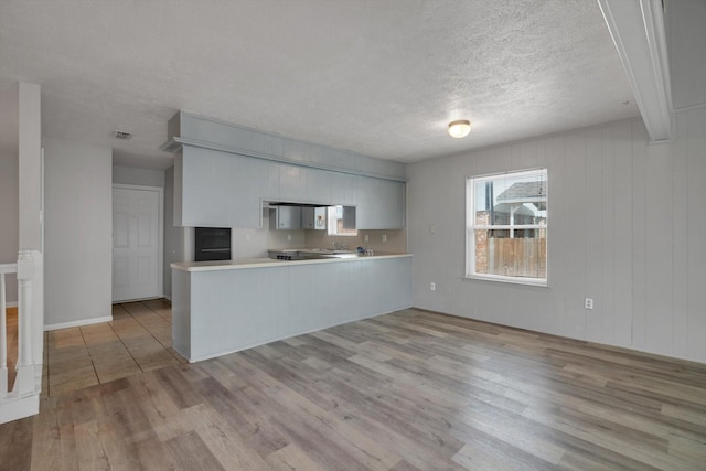 kitchen with light wood-style floors, light countertops, a peninsula, and a textured ceiling