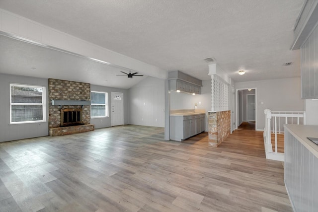 kitchen featuring ceiling fan, light wood-type flooring, a brick fireplace, and gray cabinetry