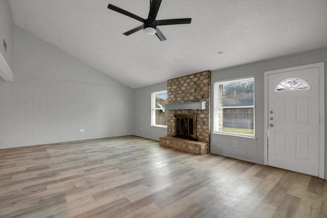 unfurnished living room with lofted ceiling, ceiling fan, wood finished floors, visible vents, and a brick fireplace