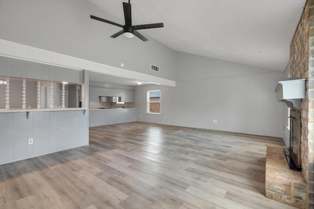 unfurnished living room featuring visible vents, ceiling fan, wood finished floors, a fireplace, and high vaulted ceiling