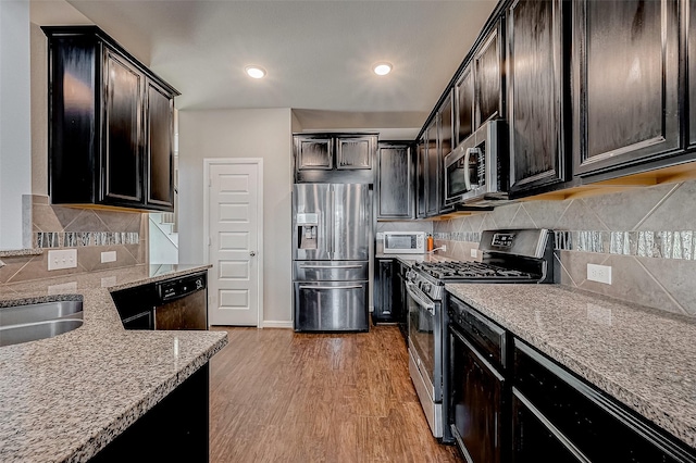 kitchen featuring light wood finished floors, stainless steel appliances, tasteful backsplash, a sink, and light stone countertops