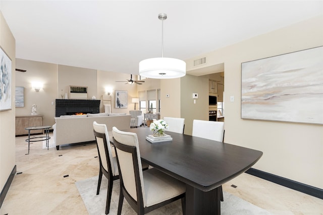 dining space featuring a warm lit fireplace, ceiling fan, visible vents, and baseboards