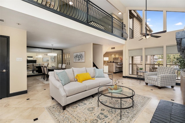 living area featuring ceiling fan, a high ceiling, visible vents, and baseboards